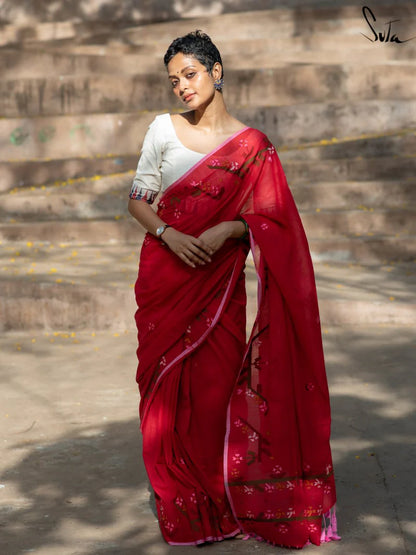 Woman wearing a red saree with a white blouse standing on stone steps.