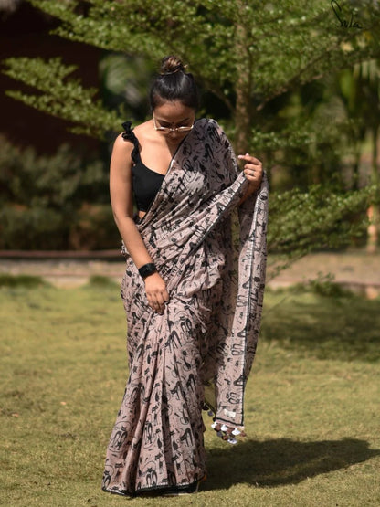 Woman wearing a patterned saree outdoors with greenery in the background