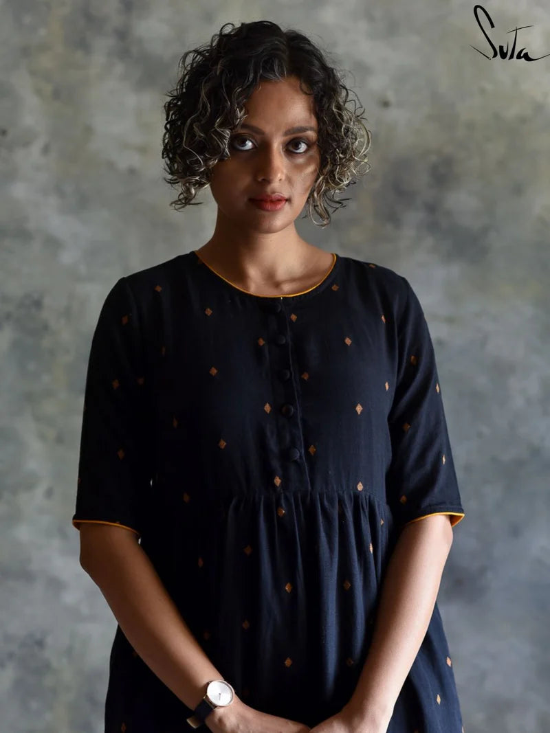 Woman wearing a black dress with gold polka dots against a textured gray background