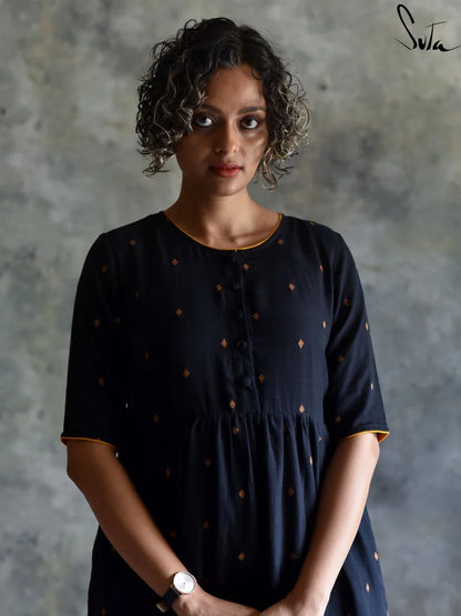 Woman wearing a black dress with gold polka dots against a textured gray background
