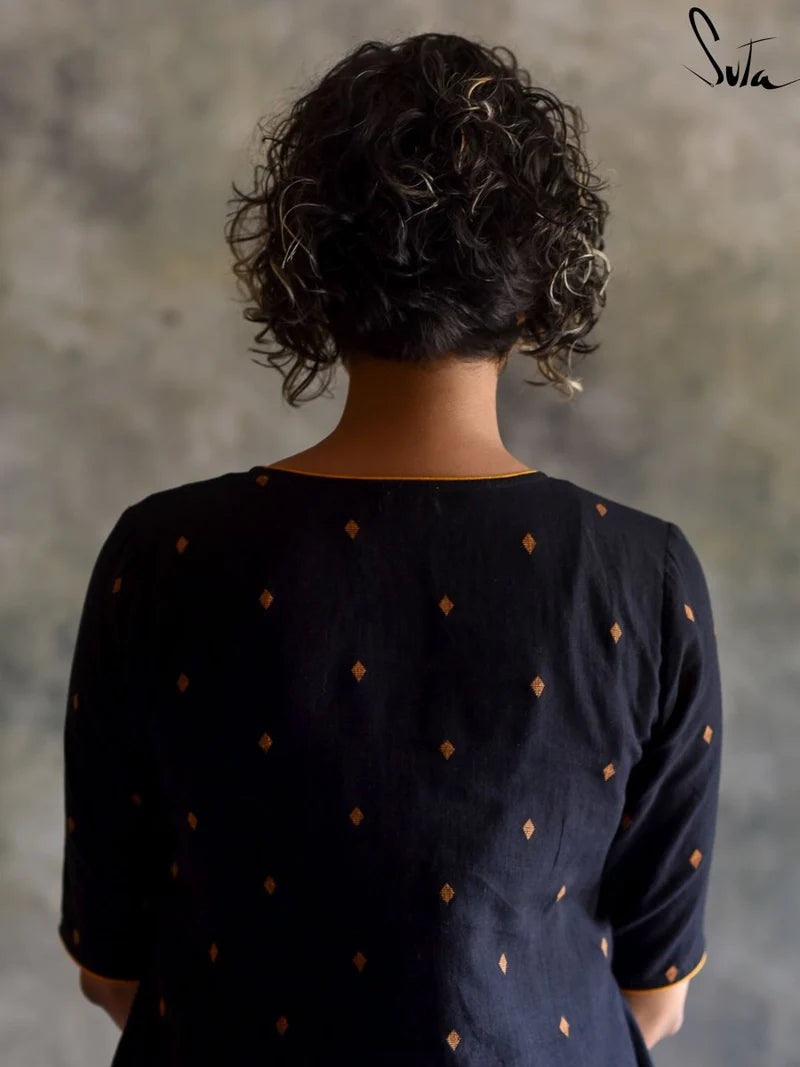Person wearing a black dress with gold polka dots against a textured gray wall.