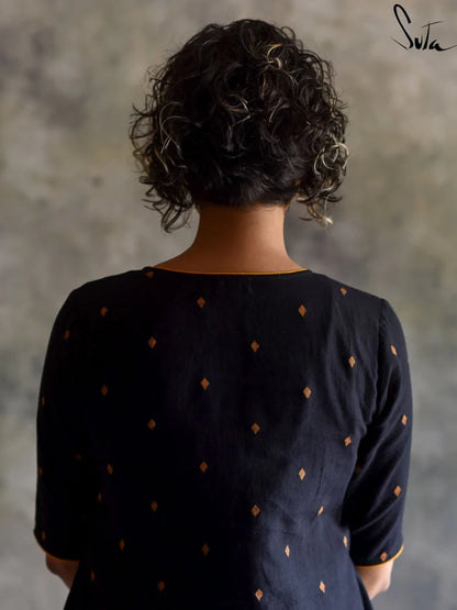 Person wearing a black dress with gold polka dots against a textured gray wall.