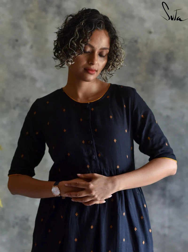 Woman wearing a black dress with gold polka dots against a gray background