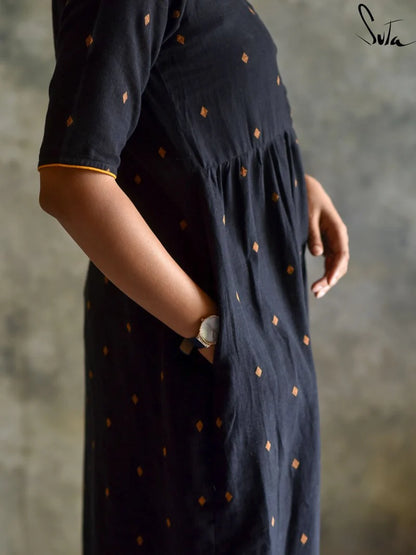 Person wearing a black dress with gold polka dots against a gray background