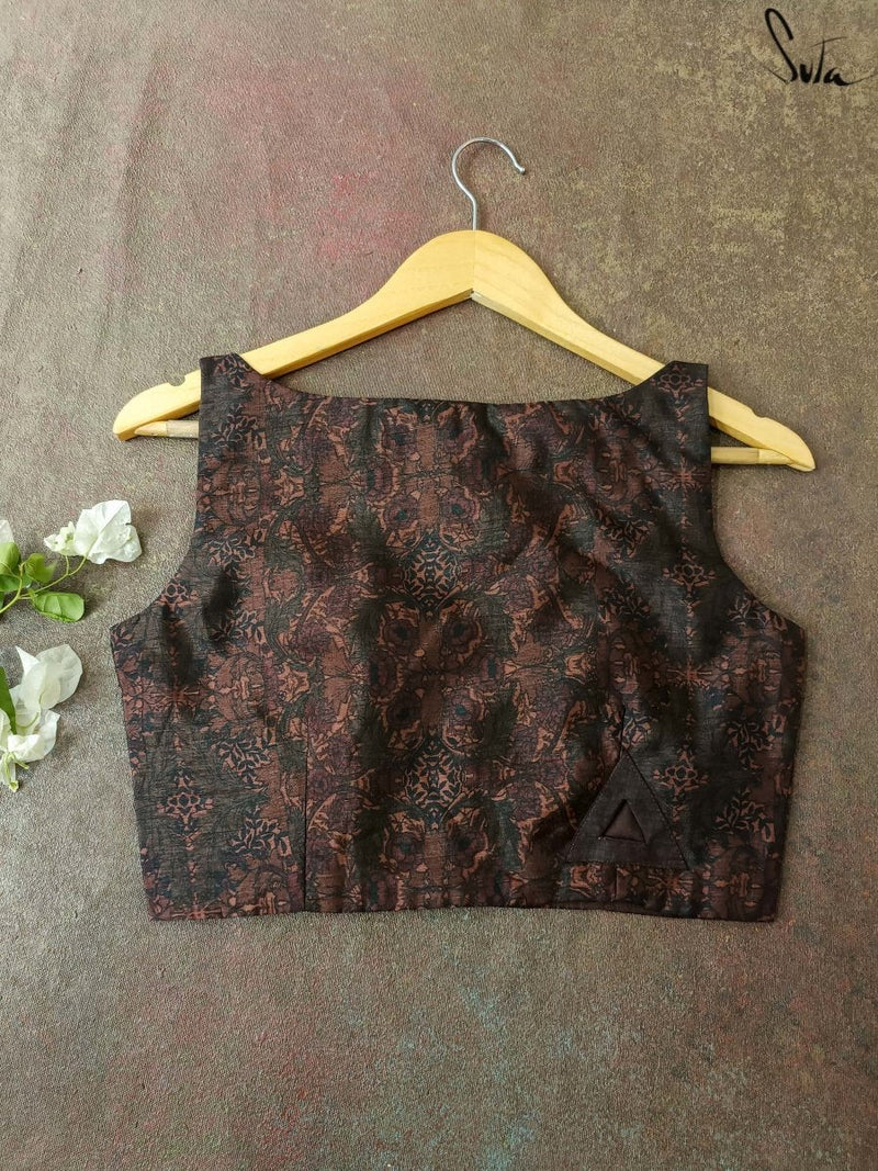 Brown patterned blouse on a hanger against a textured gray background
