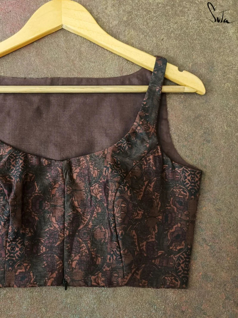 Brown patterned blouse on a hanger against a textured gray background