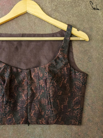 Brown patterned blouse on a hanger against a textured gray background
