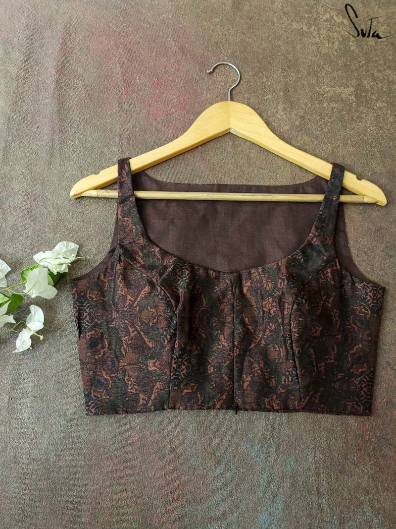 Brown patterned blouse on a hanger against a textured gray background