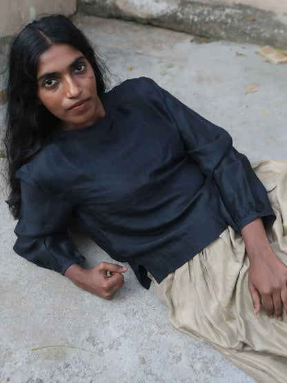 Woman sitting on a stone surface wearing a black top and beige skirt.