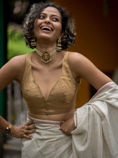 Woman wearing a gold blouse and white saree with gold jewelry.