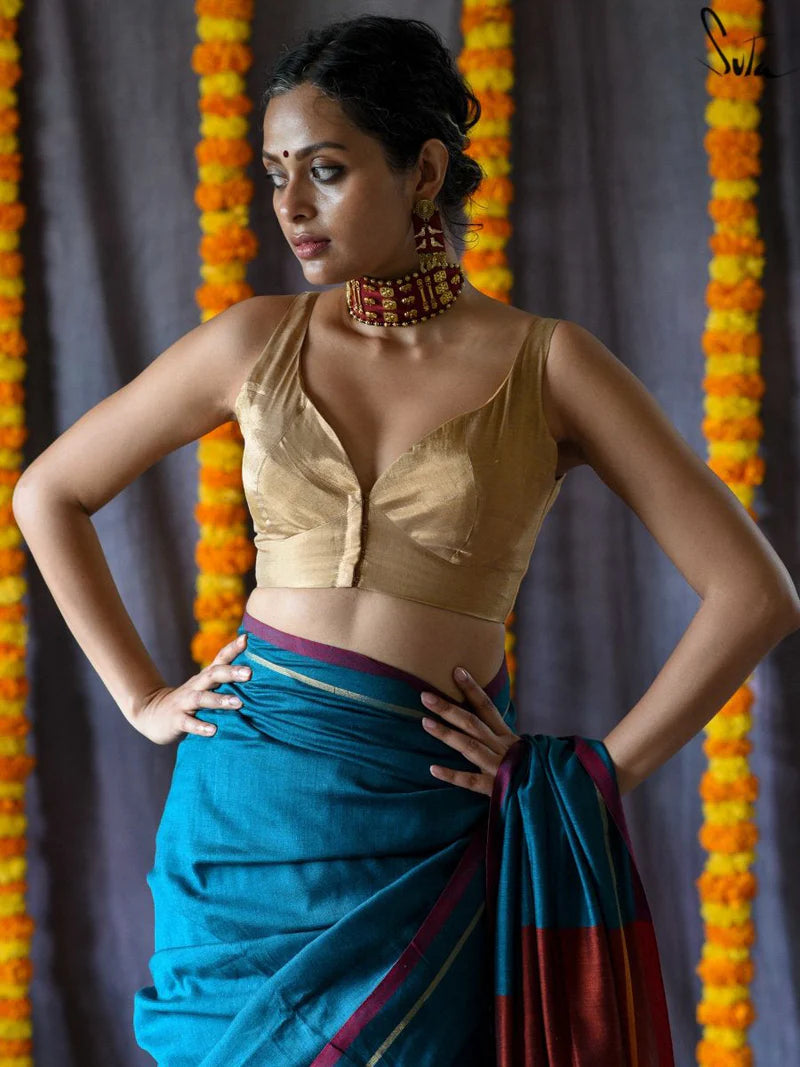 Woman in a gold blouse and blue saree with floral decorations in the background