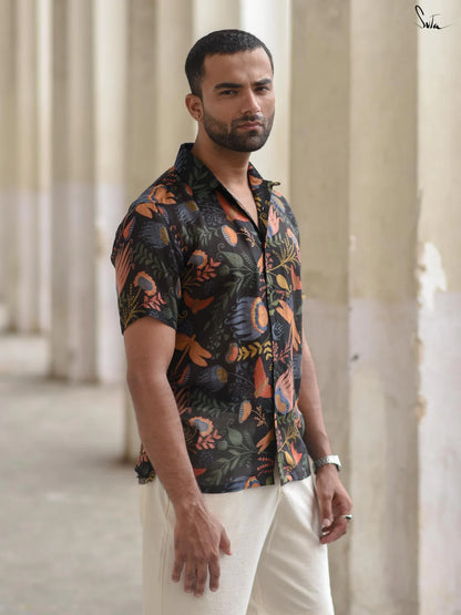 Man wearing a patterned shirt and white pants standing in front of classical architecture.