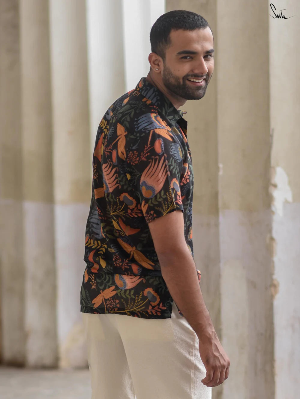 Man wearing a patterned shirt standing in front of stone columns