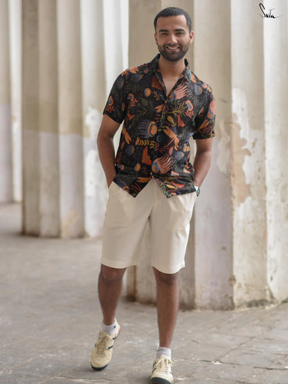 Man wearing a patterned shirt and beige shorts standing in front of columns.