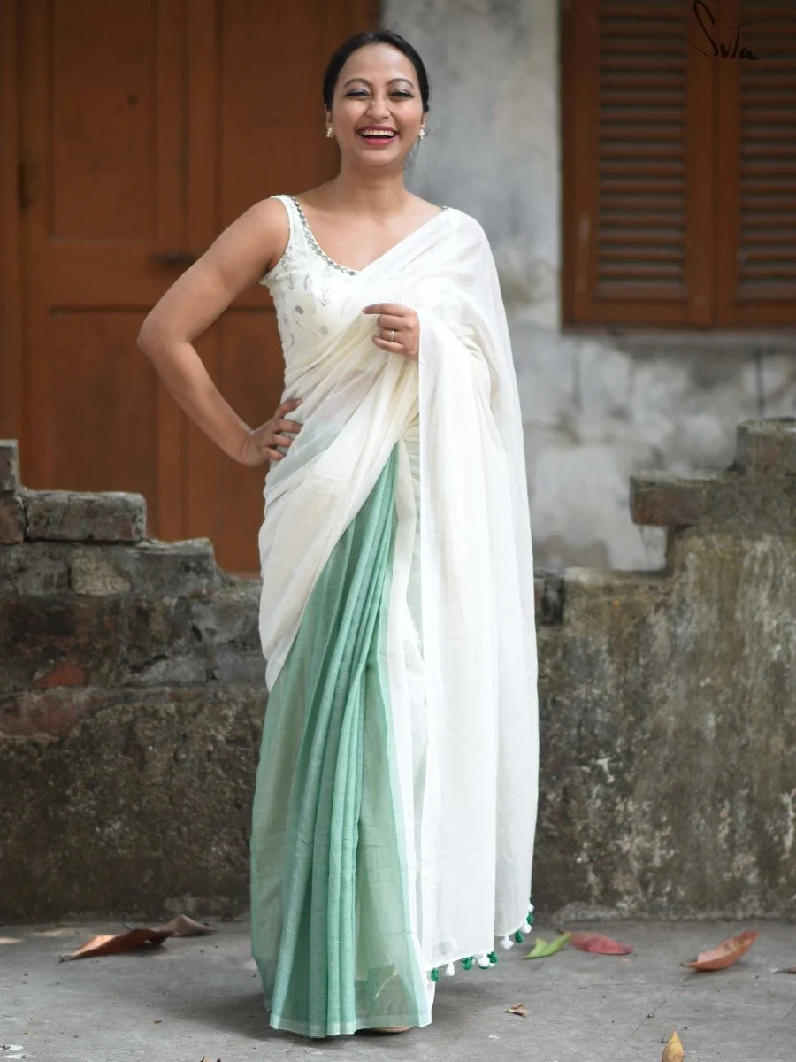 Woman wearing a white and green saree standing outdoors.