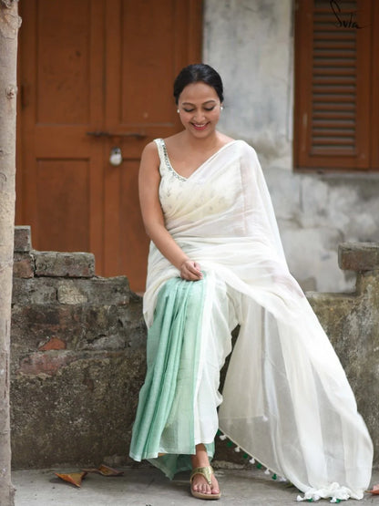 Woman in a white saree with green blouse sitting outdoors.